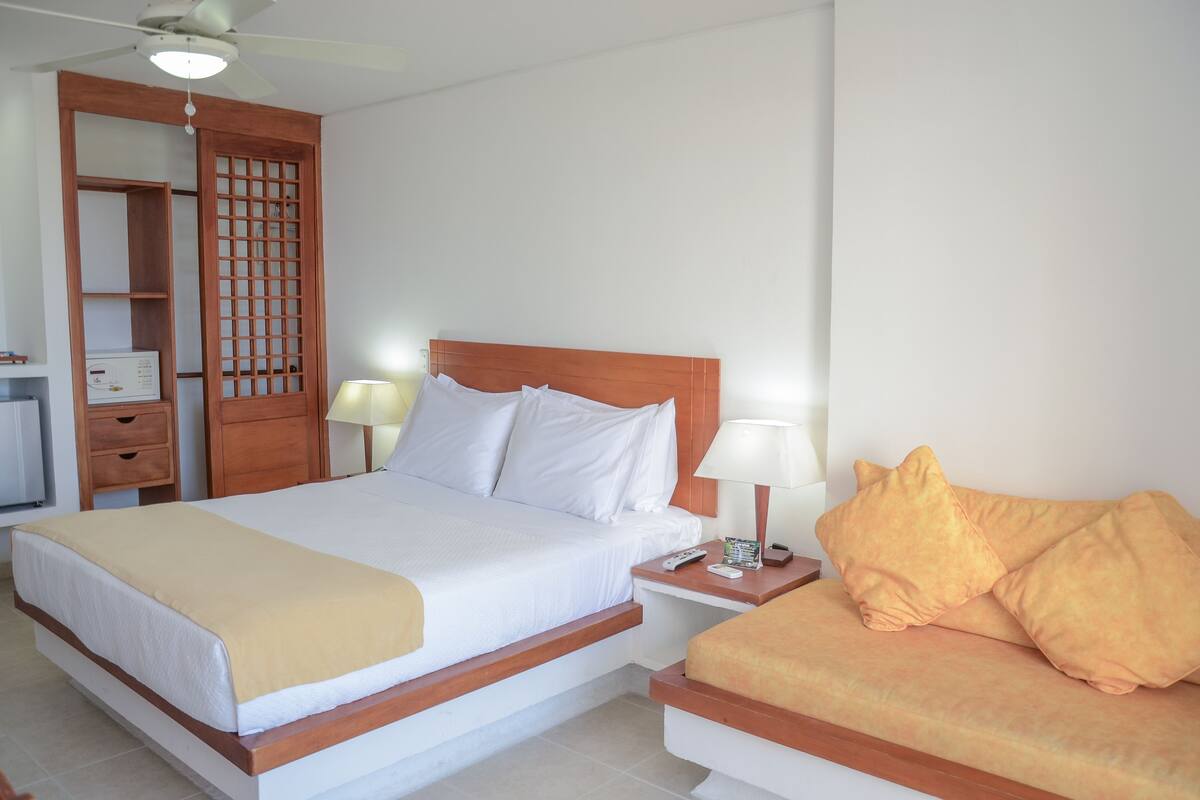 Habitación de hotel con cama, mesitas de noche, armario de madera y ventilador de techo.
