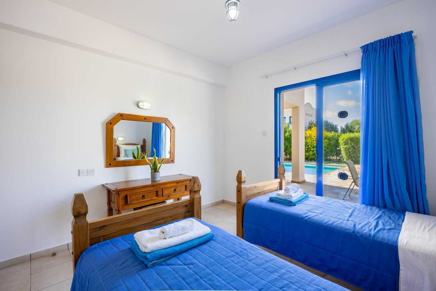 A hotel room with two beds, a wooden dresser, a mirror, and a view of a swimming pool.
