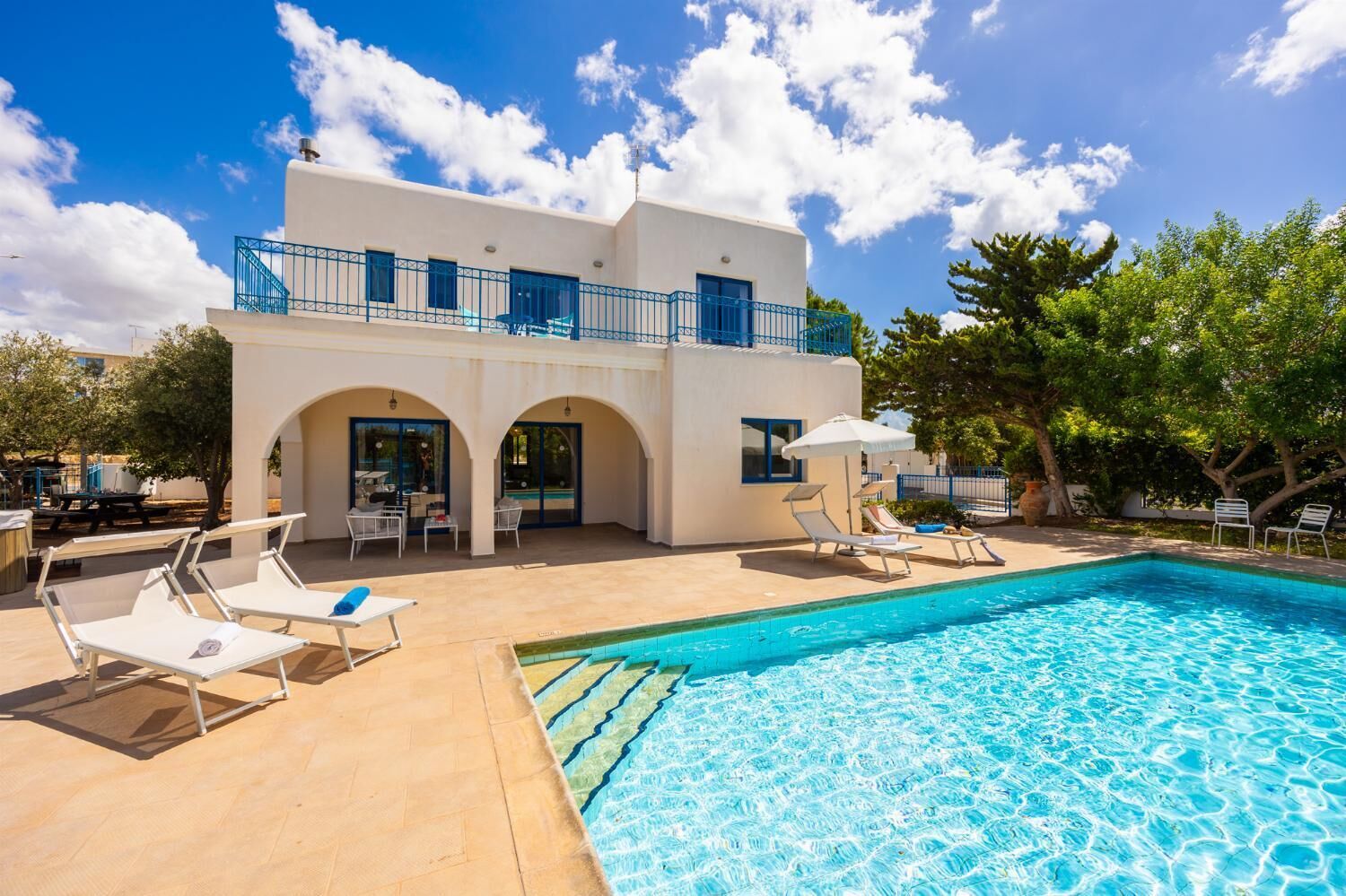 A two-story building with a swimming pool, outdoor seating, and a clear blue sky.