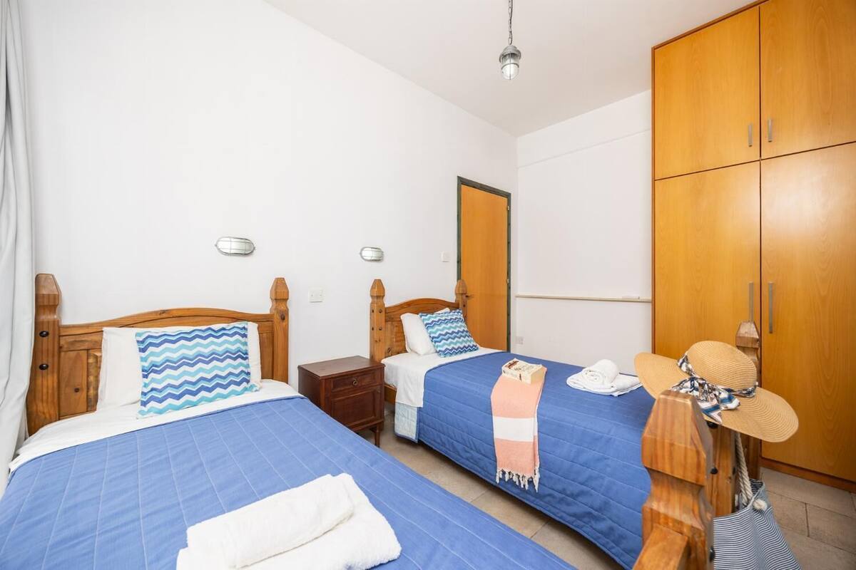 Een hotelkamer met twee bedden, houten kasten en een klein tafeltje met een hoed en handdoek.