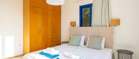 Habitación de hotel con una cama grande, armario de madera, dos lámparas de noche, una ventana con cortinas y una pequeña mesa redonda.