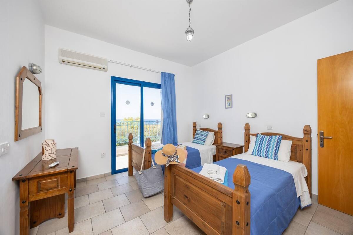 Een slaapkamer met twee houten bedden, een nachtkastje van hout, een spiegel en een raam met blauwe gordijnen.