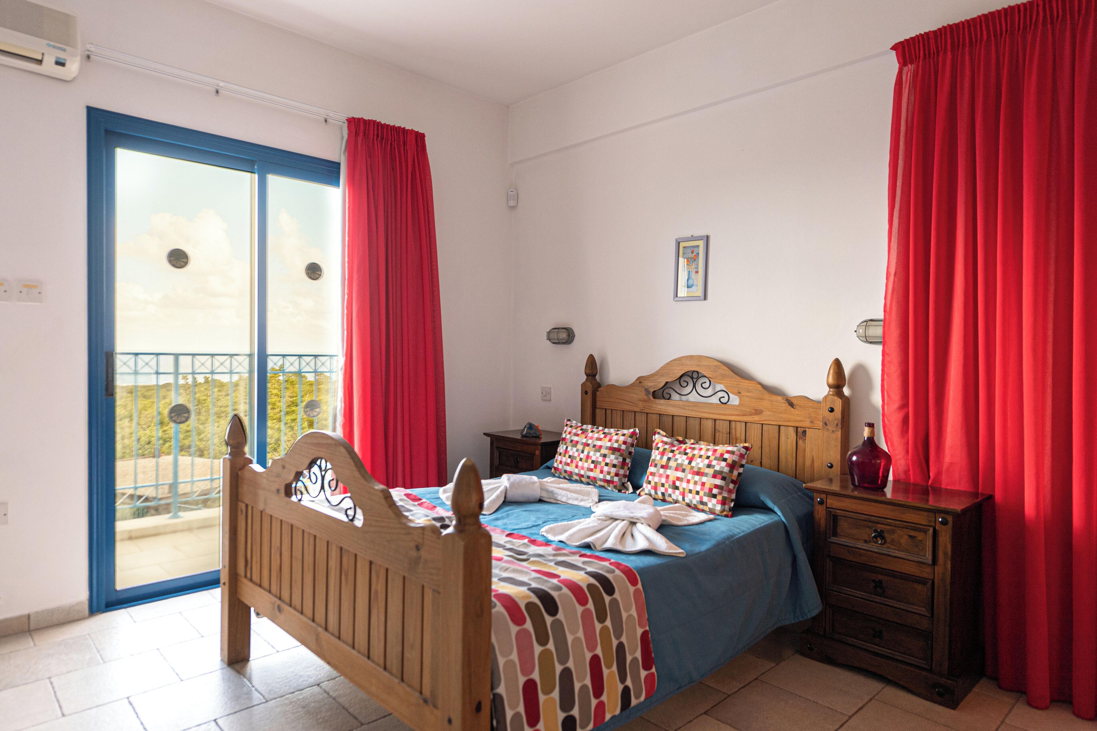 A bedroom with a wooden bed, a nightstand, a dresser, and a balcony with red curtains.