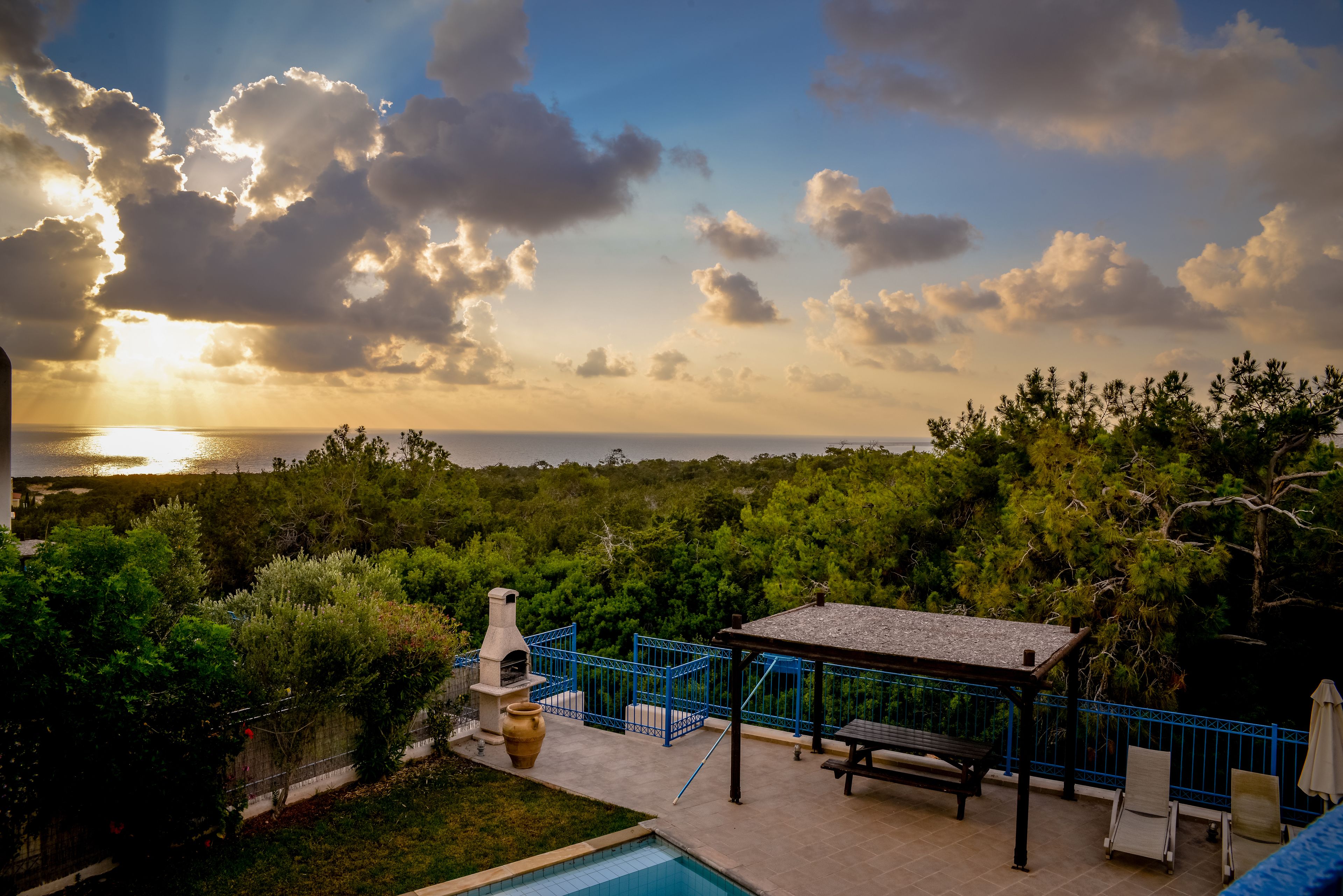 A backyard with a barbecue grill, a pool, and a gazebo overlooking a forested area.