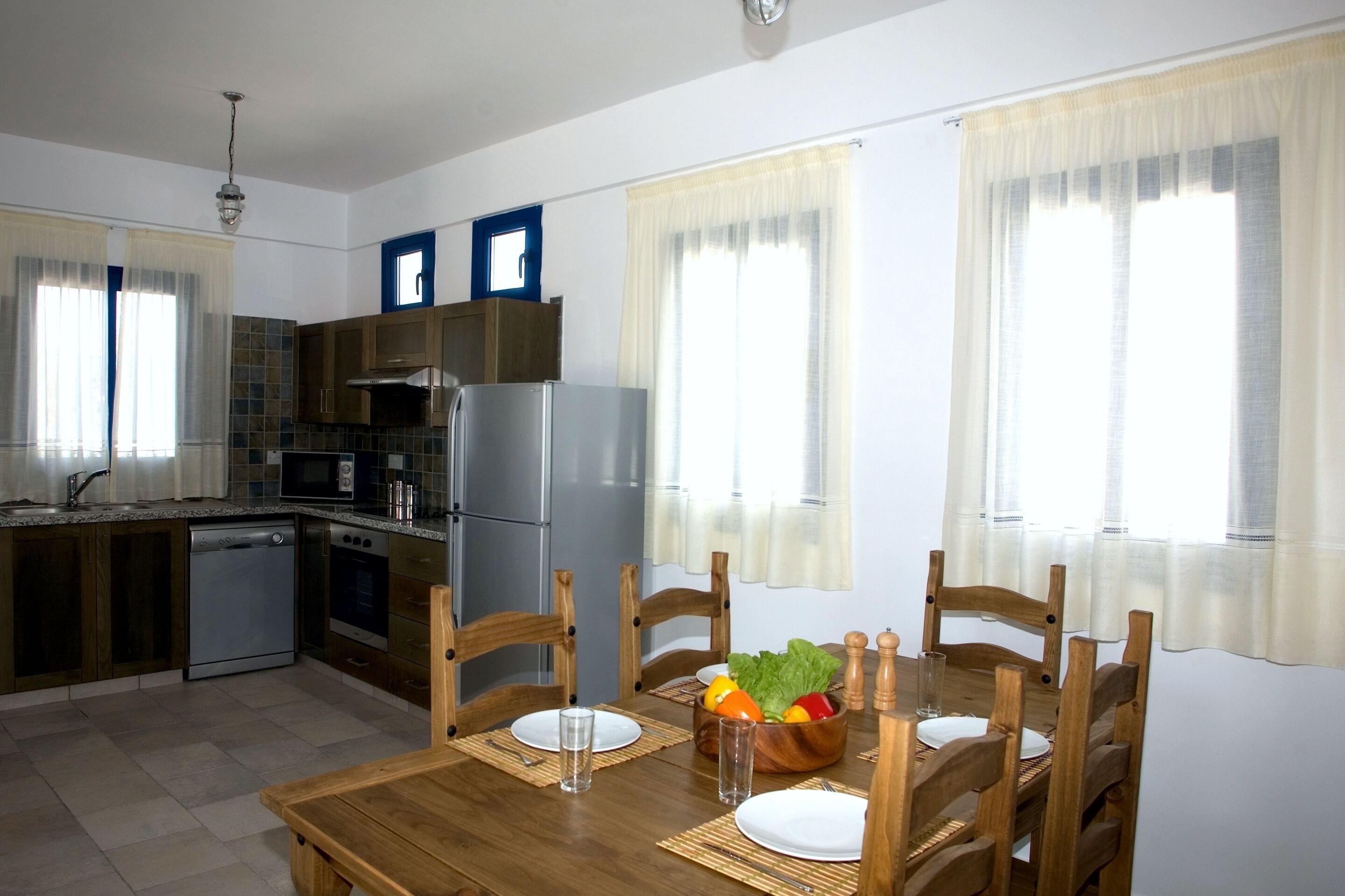 Una cucina compatta con zona pranzo, che include un tavolo di legno apparecchiato per due persone, un frigorifero, un forno a microonde ed una lavastoviglie.