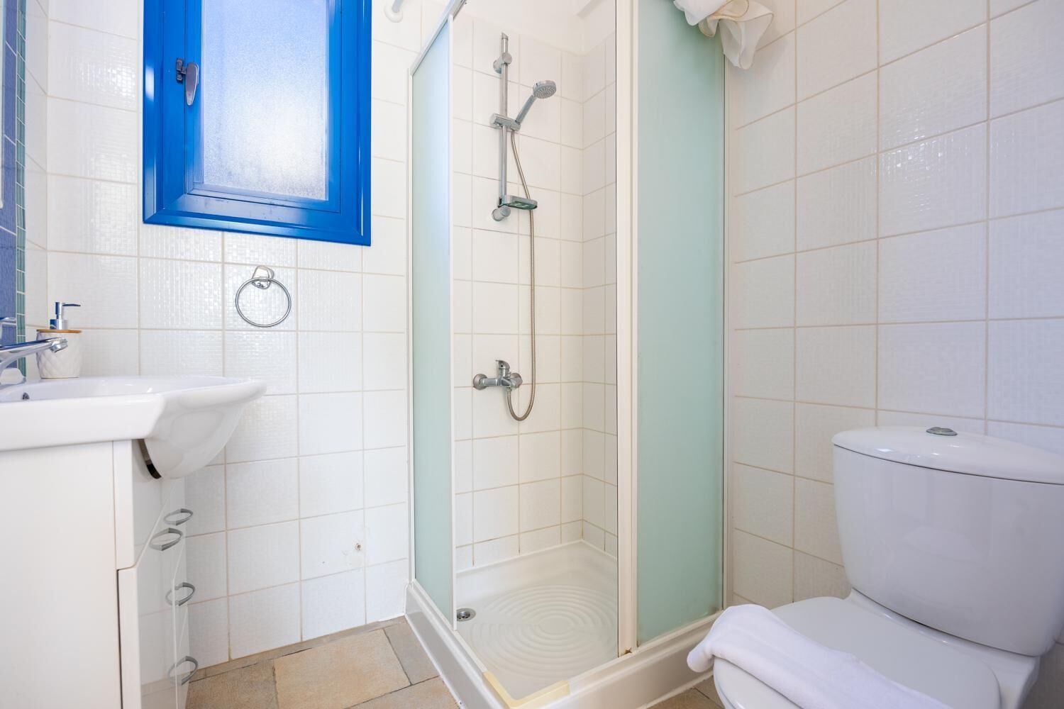 A bathroom with a white sink, a blue-framed mirror, a glass-enclosed shower, and a white toilet.