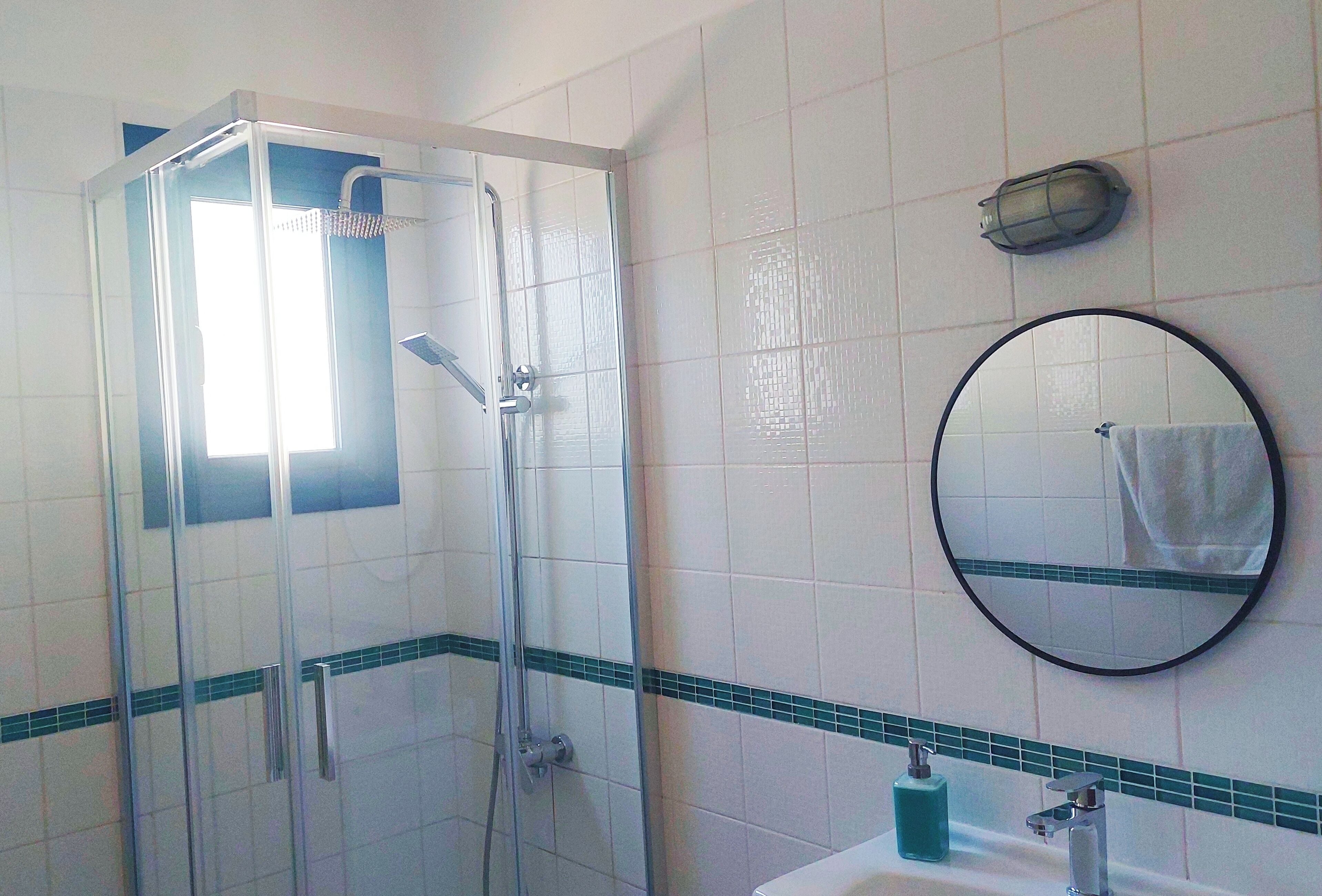 A bathroom with a glass-enclosed shower, a sink with a mirror, and a towel hanging on the wall.