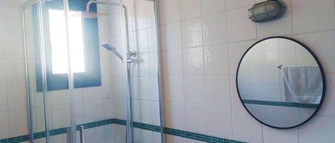 A bathroom with a glass-enclosed shower, a sink with a mirror, and a towel hanging on the wall.