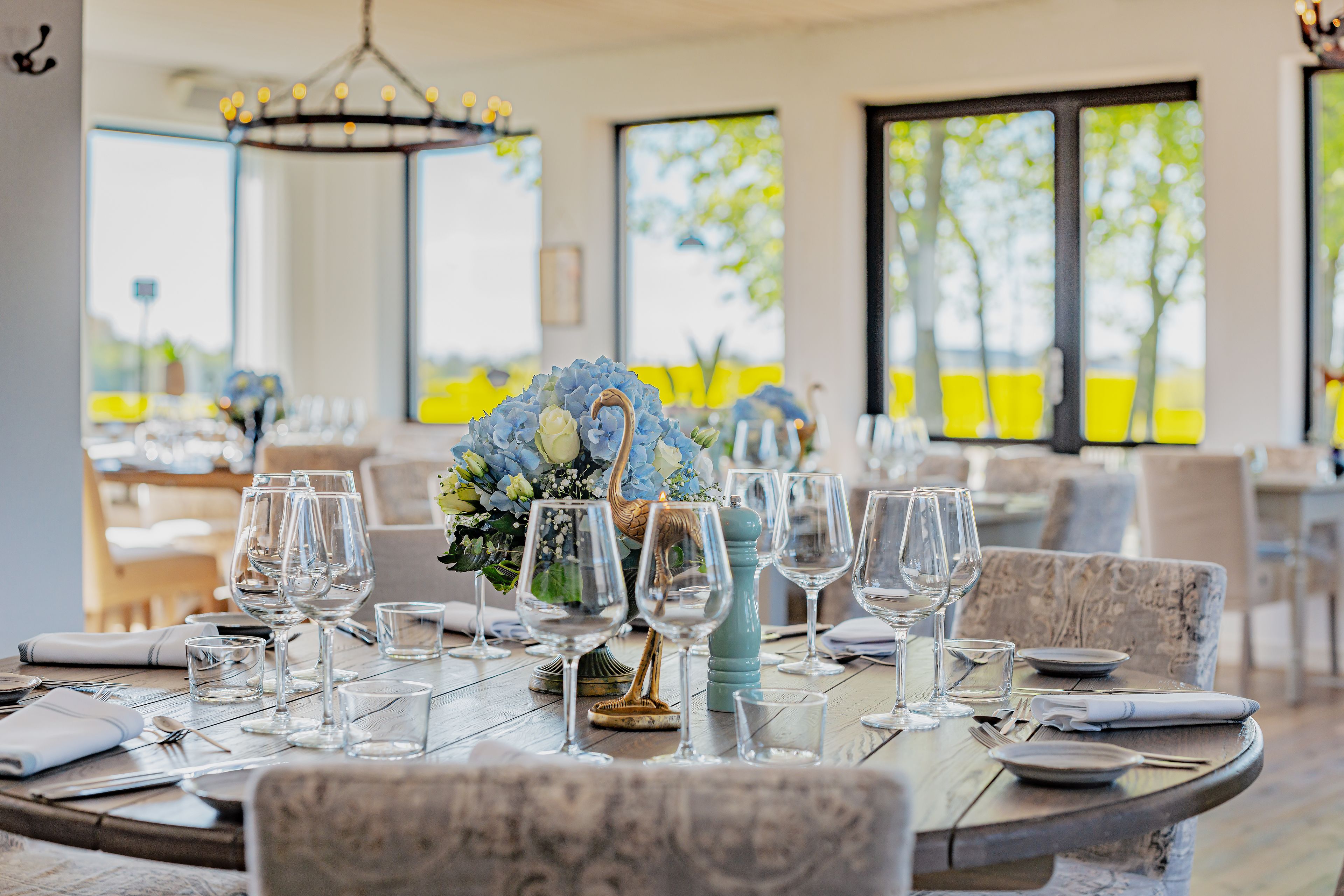 Une table à manger dressée avec de nombreux verres à vin, des assiettes et des couverts, entourée de chaises.