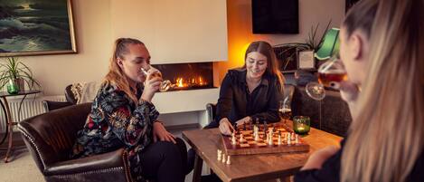 Un salon chaleureux avec une cheminée, un jeu d’échecs et un téléviseur fixé au mur.
