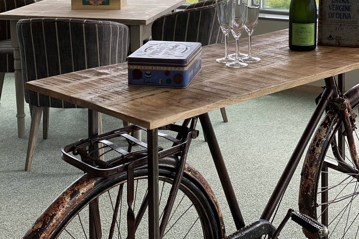 A dining table with a chessboard, wine glasses, and a bottle of wine. A bicycle is parked in front of the table.