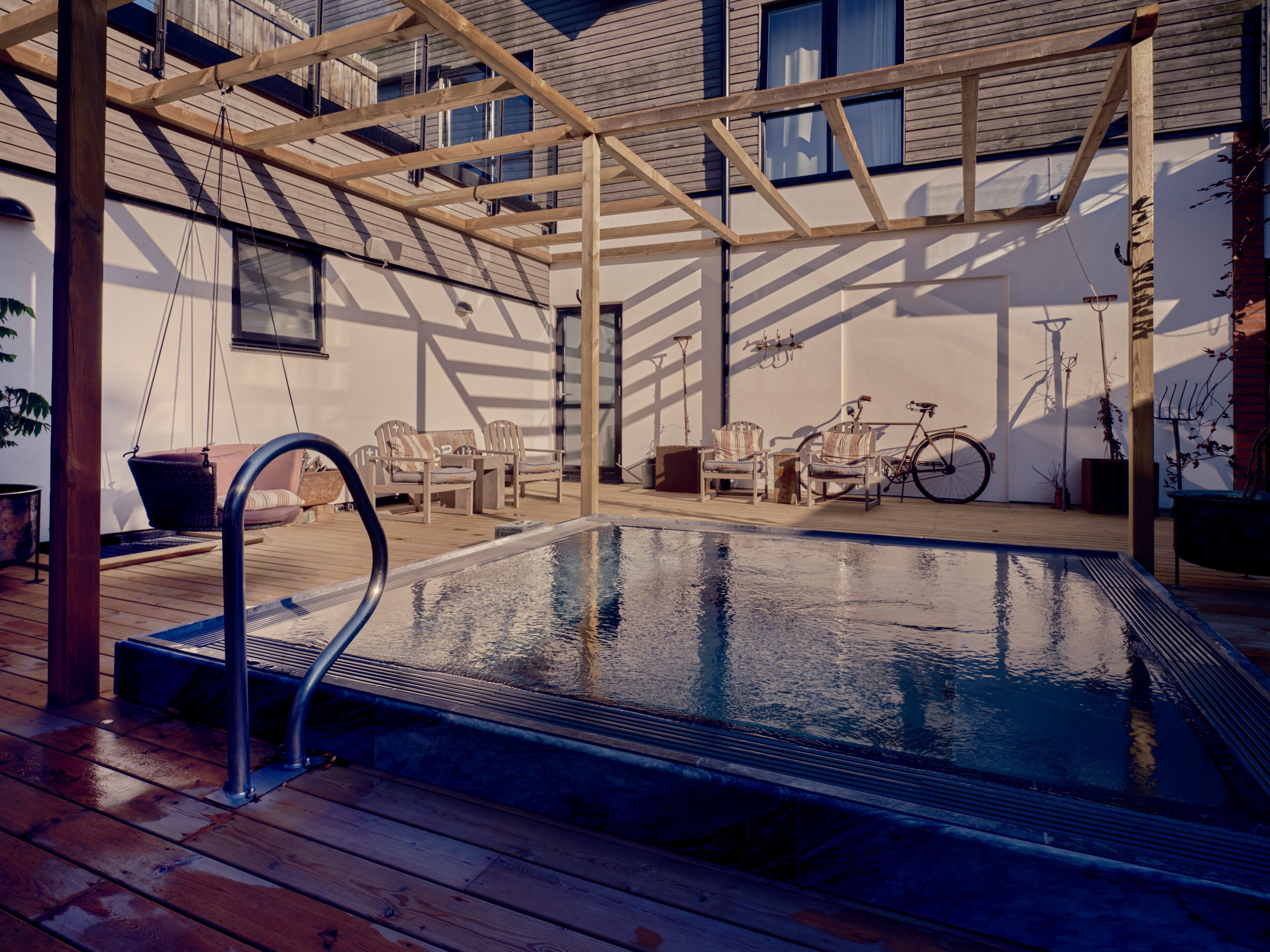 A wooden deck with a swimming pool, outdoor furniture, and a bicycle.