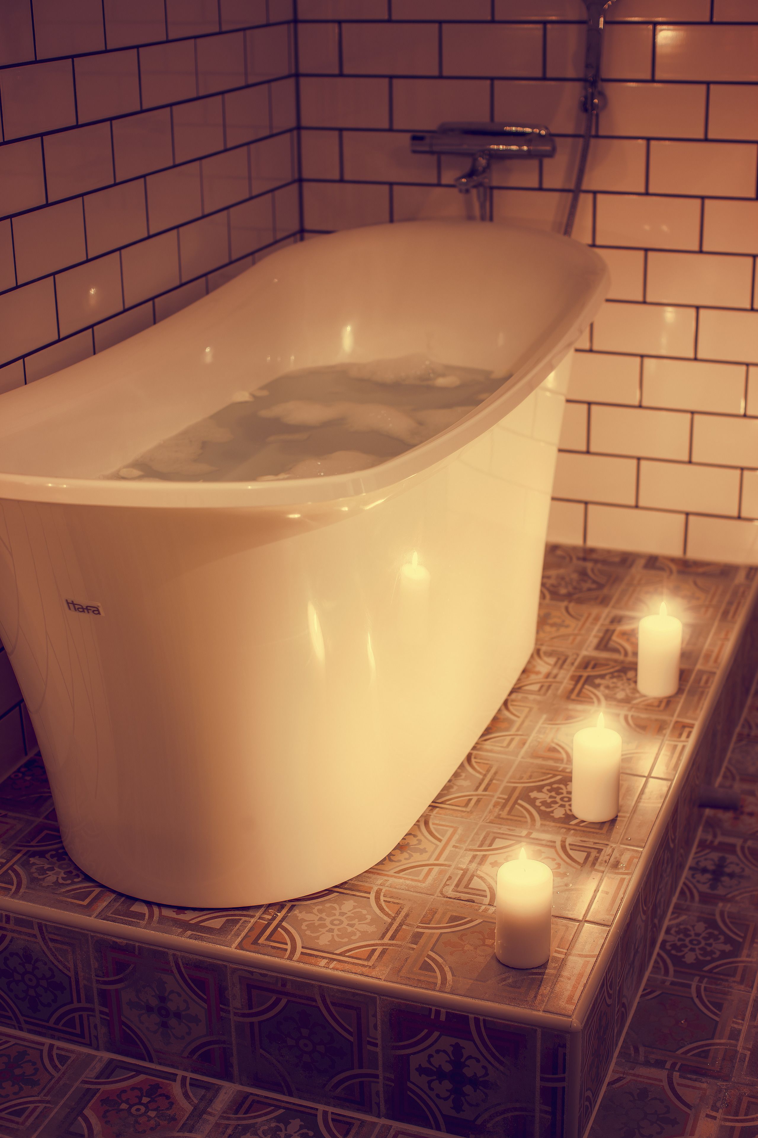 A bathtub with a faucet and a showerhead, surrounded by patterned tiles.