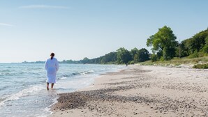 Una playa con una persona vestida de blanco caminando por la orilla.