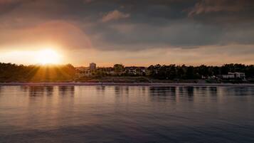 Ein Sonnenuntergang über ruhigem Wasser, im Hintergrund Gebäude und Bäume.