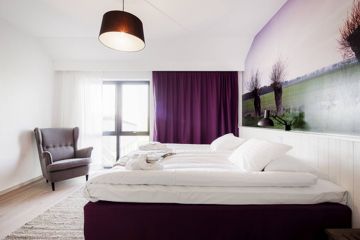 A bedroom with a bed, a chair, a window, and a painting on the wall.