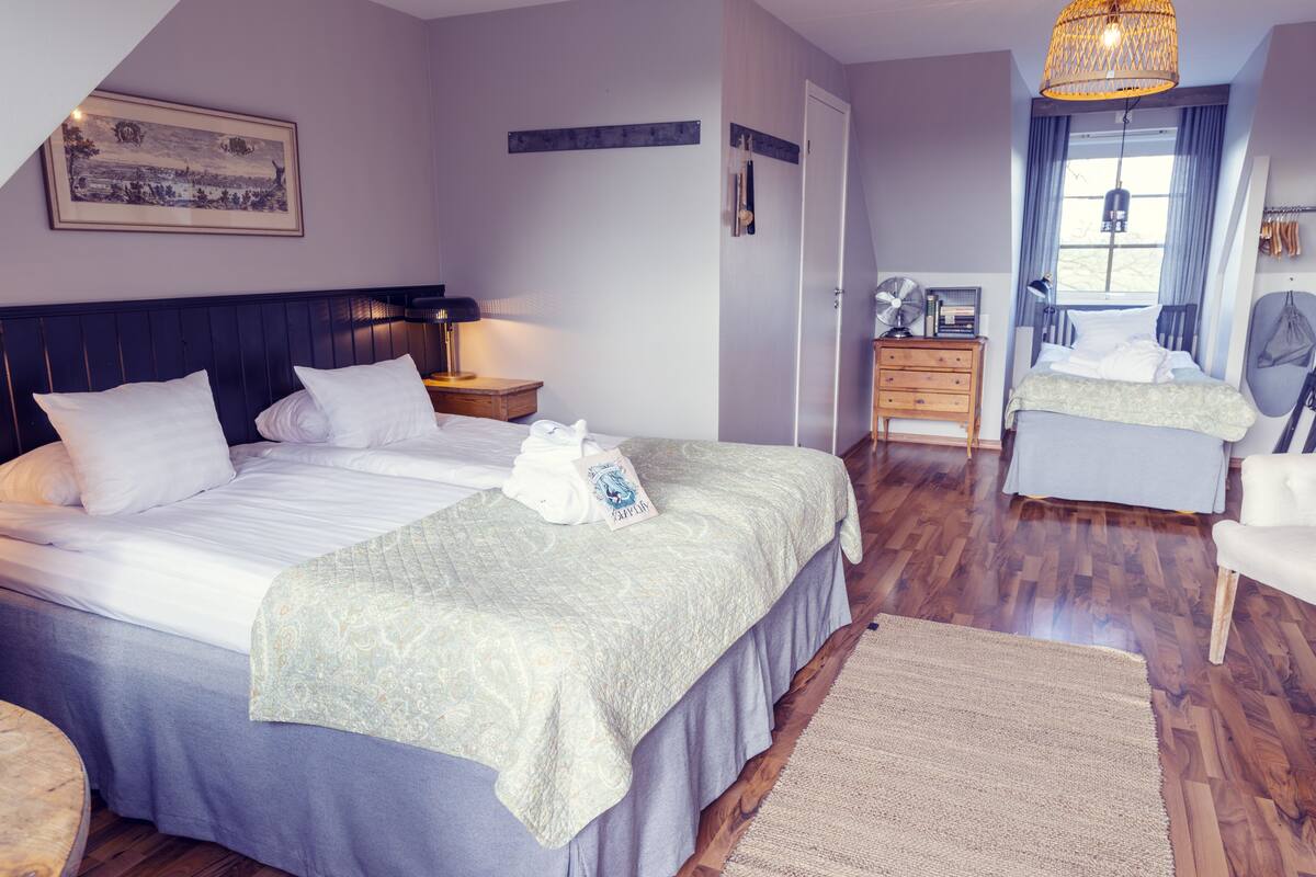 A bedroom with a bed, bedside table, lamp, and a dresser.