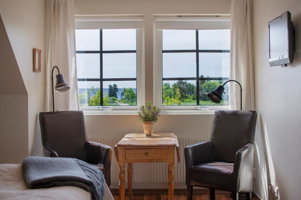 Ett sovrum med två stolar, ett litet bord med en växt och en säng.