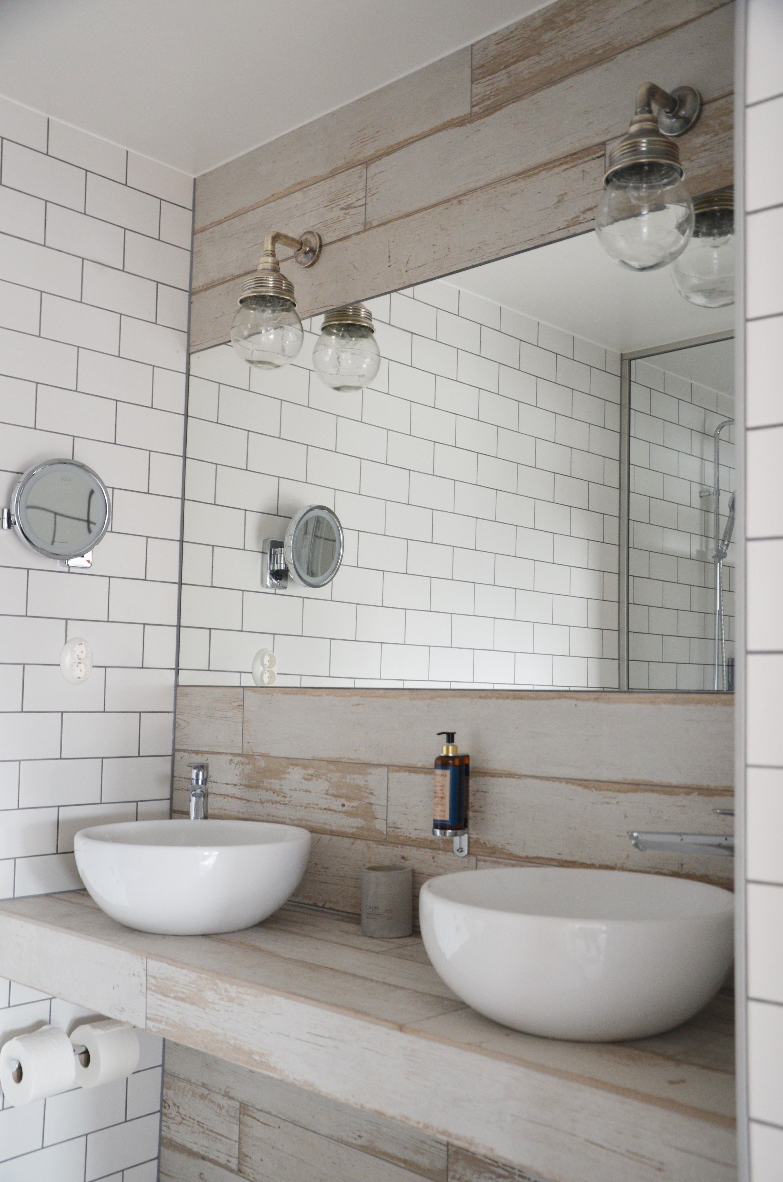 Ein Badezimmer mit zwei weißen Waschbecken, einer Wand mit Holzverkleidung und einem großen Spiegel.