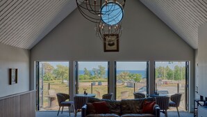 Un vaste espace de vie doté d’un haut plafond, d’un lustre moderne et d’une grande fenêtre offrant une vue sur l’extérieur.
