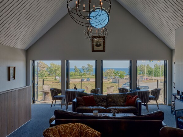 A spacious living area with a high ceiling, a modern chandelier, and a large window offering a view of the outdoors. - Hotell Mossbylund (Skivarp)