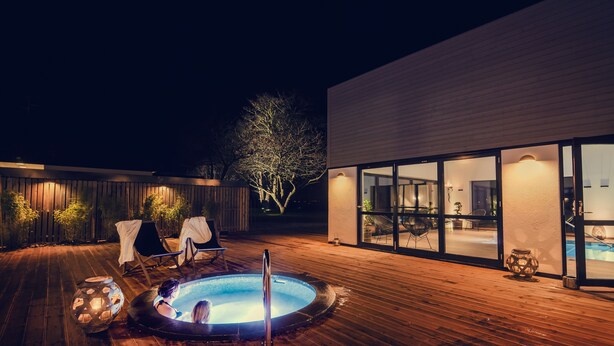 Un espace extérieur avec piscine, un jacuzzi, une terrasse en bois et un bâtiment moderne doté de portes vitrées.