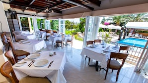 A restaurant with outdoor seating overlooking a pool, featuring white tablecloths and wooden chairs. - Fitos Inn Guest House (Geroskipou)