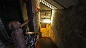A narrow stone staircase with a wooden handrail, leading to a lit area at the top. - XIV Century rooms (Kastela)