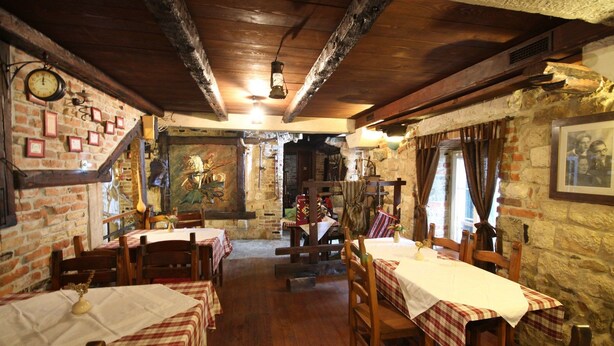 A rustic dining area with wooden tables and chairs, stone walls, and exposed wooden beams. - XIV Century rooms (Kastela)