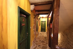 A narrow hallway with stone flooring, wooden beams, and green doors. - XIV Century rooms (Kastela)