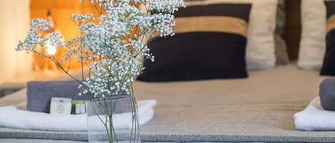 Una cama con almohadas y una mesita de noche con un florero y revistas.