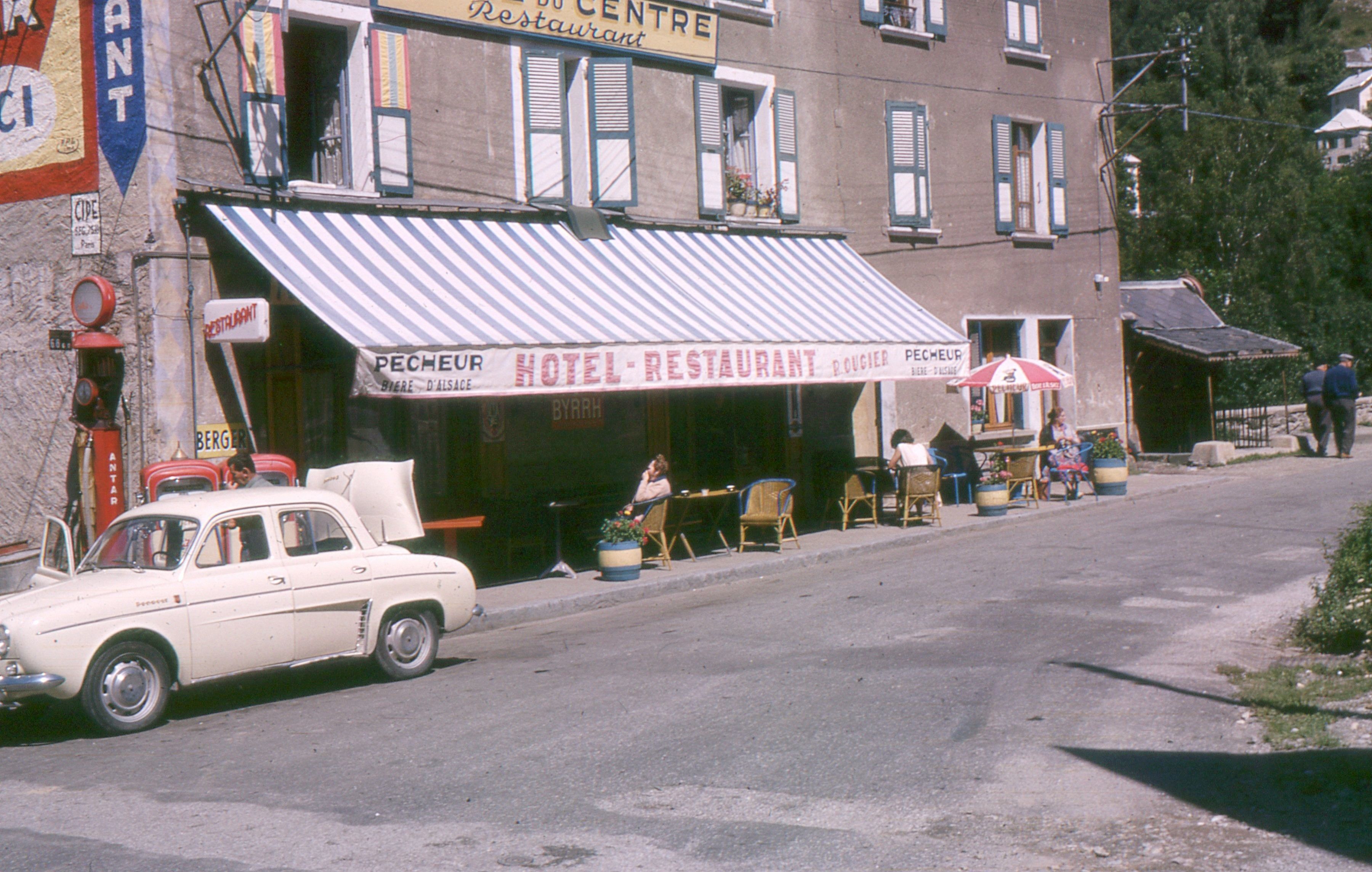 A hotel with a striped awning, outdoor seating, and a parked car.
