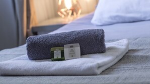 A neatly made bed with a rolled towel and a bottle of lotion on a white towel.