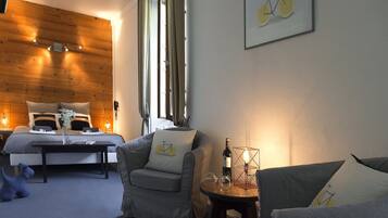 A cozy room with a bed, a grey sofa, a small table with a bottle and glasses, and a wall-mounted bicycle artwork.