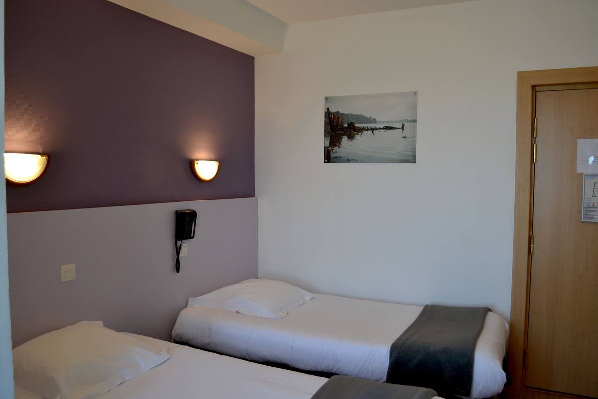 Ett hotellrum med två sängar, en telefon på väggen och en tavla som föreställer ett landskap.