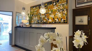 A reception area with a large mural, a counter with a lamp, and white orchids. - Hotel De La Porte Saint Pierre (Saint-Malo)