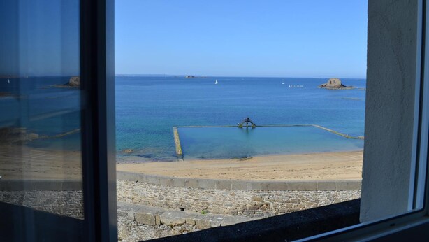 A coastal view from a window, including a sandy beach, calm sea, and distant rocky outcrops. - Hotel De La Porte Saint Pierre (Saint-Malo)
