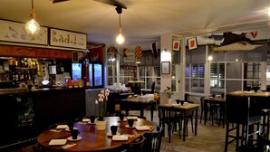 A restaurant with wooden tables and chairs, a bar area with bottles and a TV, and framed artwork on the walls. - Hotel De La Porte Saint Pierre (Saint-Malo)