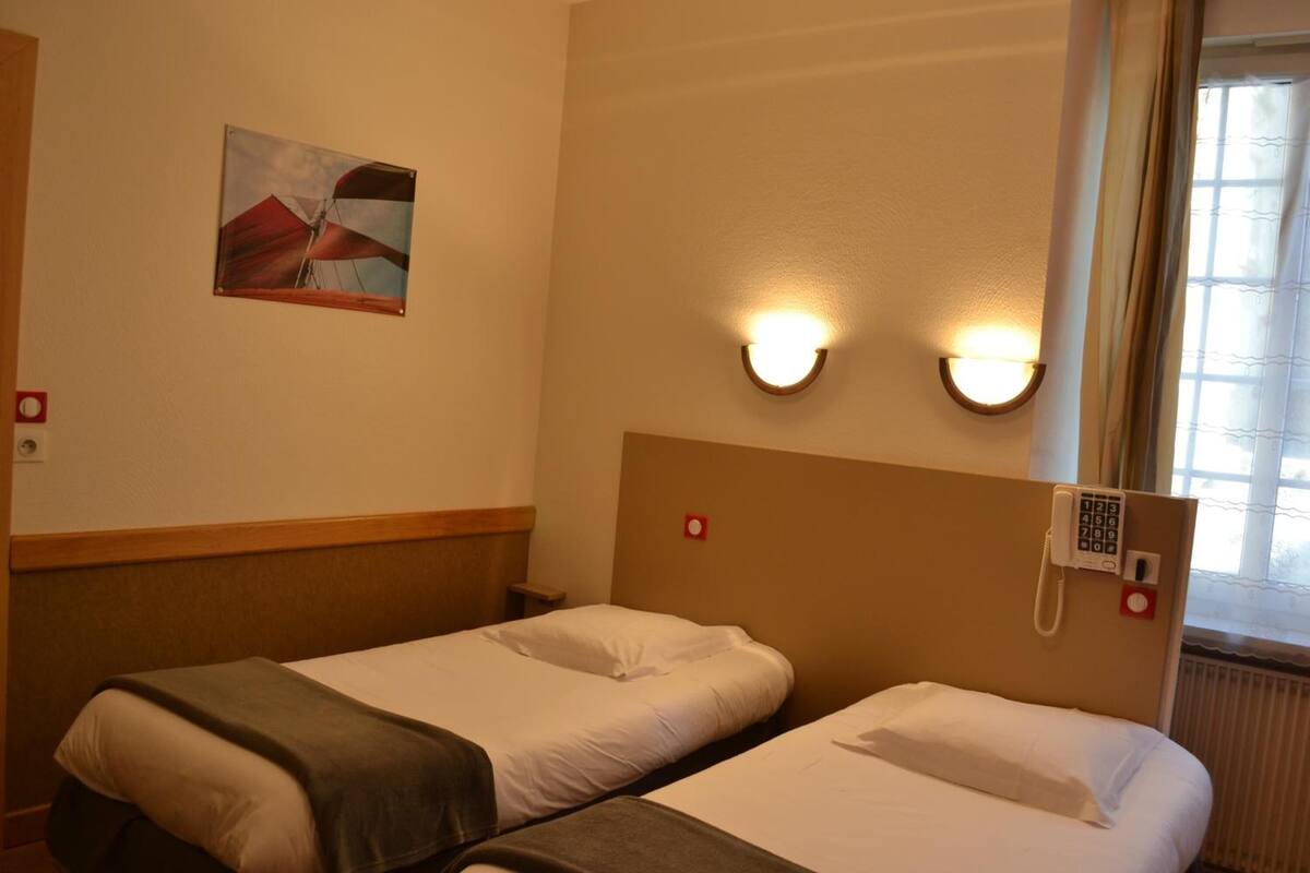 Ett hotellrum med två separata sängar, en tavla på väggen och en telefon på sänggaveln.