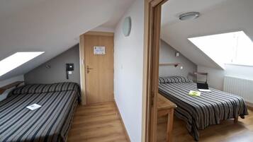 Une chambre de dortoir avec deux lits simples, une porte en bois, une petite table et un puits de lumière.
