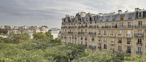 A row of multi-story buildings with balconies and a dense tree line in the foreground.