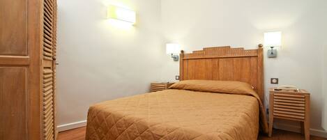 Un dormitorio con cabecera de madera, colcha acolchada, dos mesitas de noche con lámparas y suelo de madera.