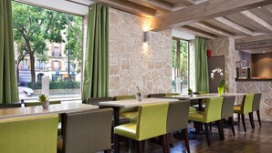 Restaurante com paredes de pedra, cortinas verdes e vista para a rua.