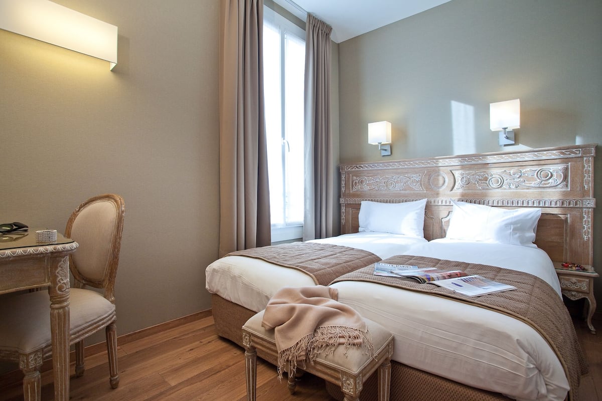 A hotel room with a large bed, two bedside lamps, a wooden headboard, a chair, and a small table with a lamp.