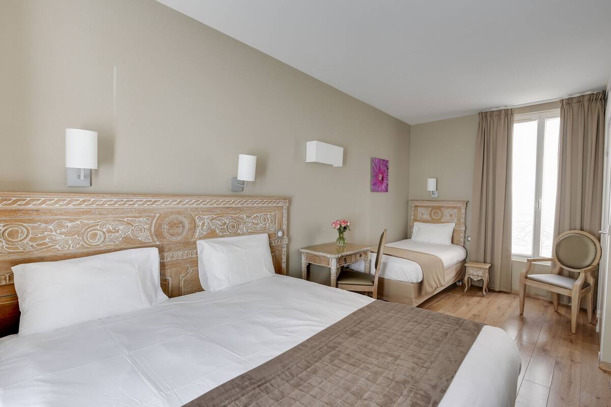 A hotel room with a large bed, a smaller bed, a desk with a chair, a round table, and a chair.