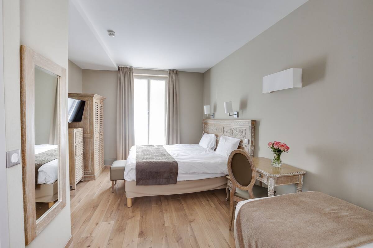 A bedroom with a bed, a bedside table with a vase of flowers, a chair, a television, and a wardrobe.