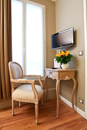 A room with a wooden chair, a small table with a vase of flowers, a flat-screen TV, and a window with curtains. - Hôtel du Printemps (Paris)