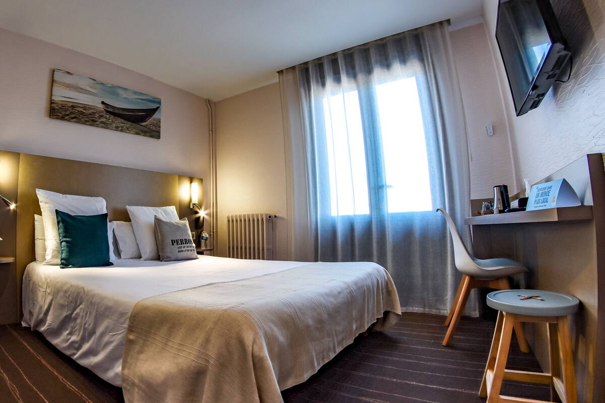 A hotel room with a large bed, a desk, a chair, a television, and a window with curtains.