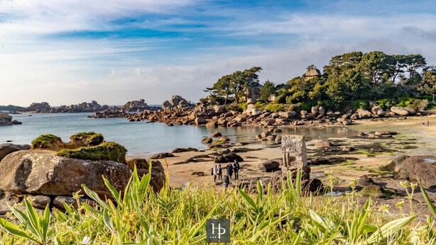A rocky beach with large boulders, a clear sky, and a few people walking. - Hotel Du Parc (Perros-Guirec)