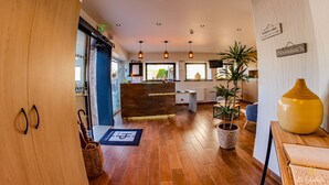 A hotel lobby with wooden flooring, a reception desk, potted plants, and a large vase. - Hotel Du Parc (Perros-Guirec)